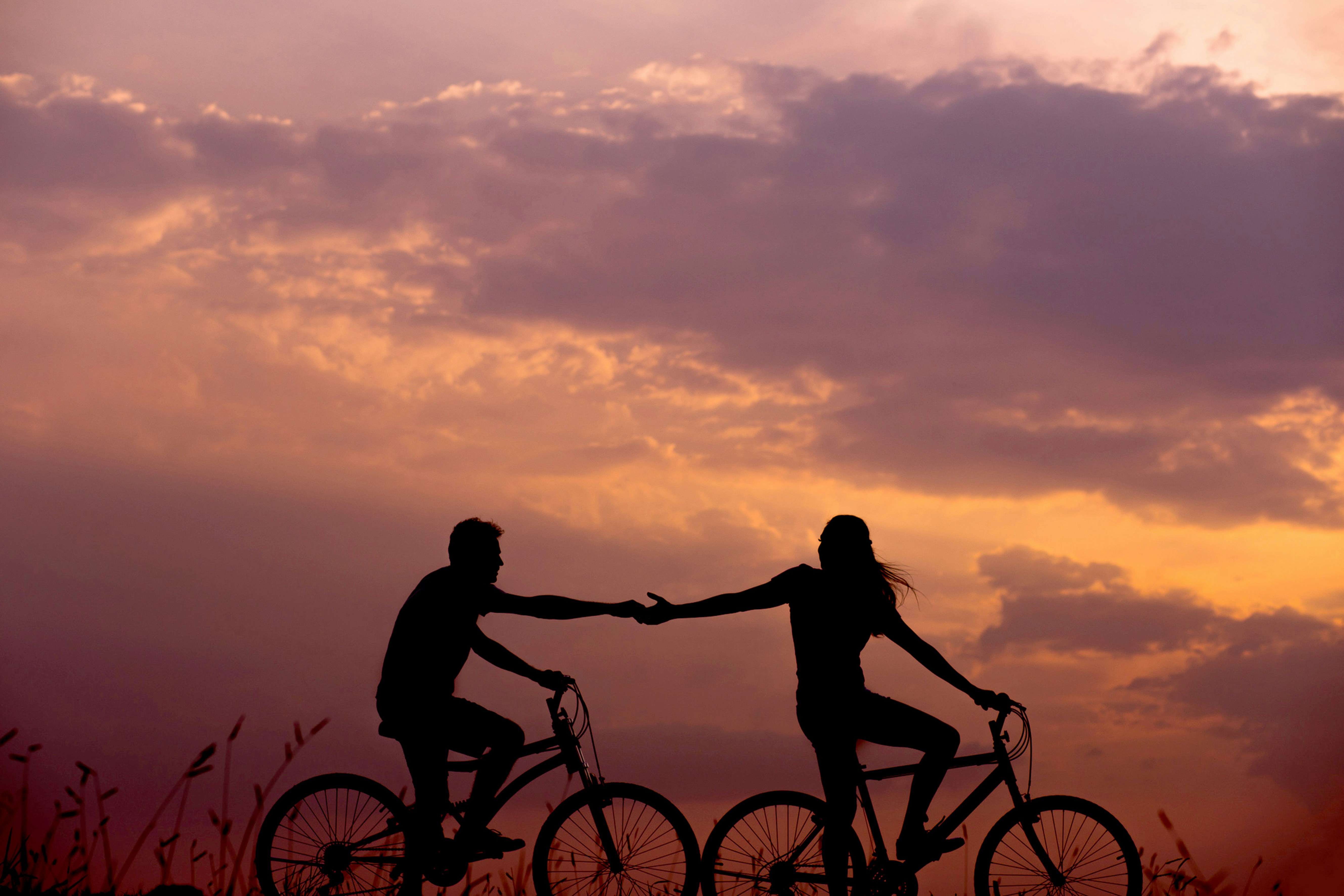 Two people cycling along a beach with the sunsetting