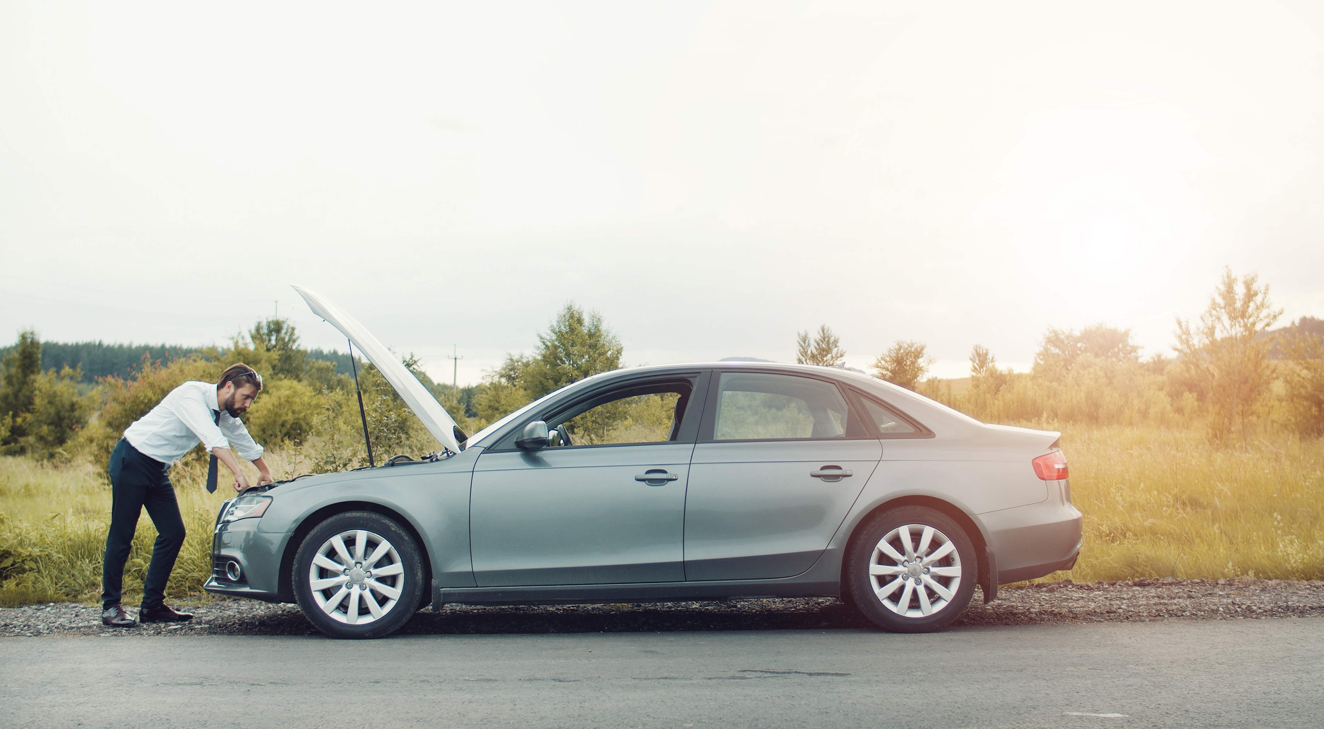 Man looking at bonnet of broken down car in the countryside