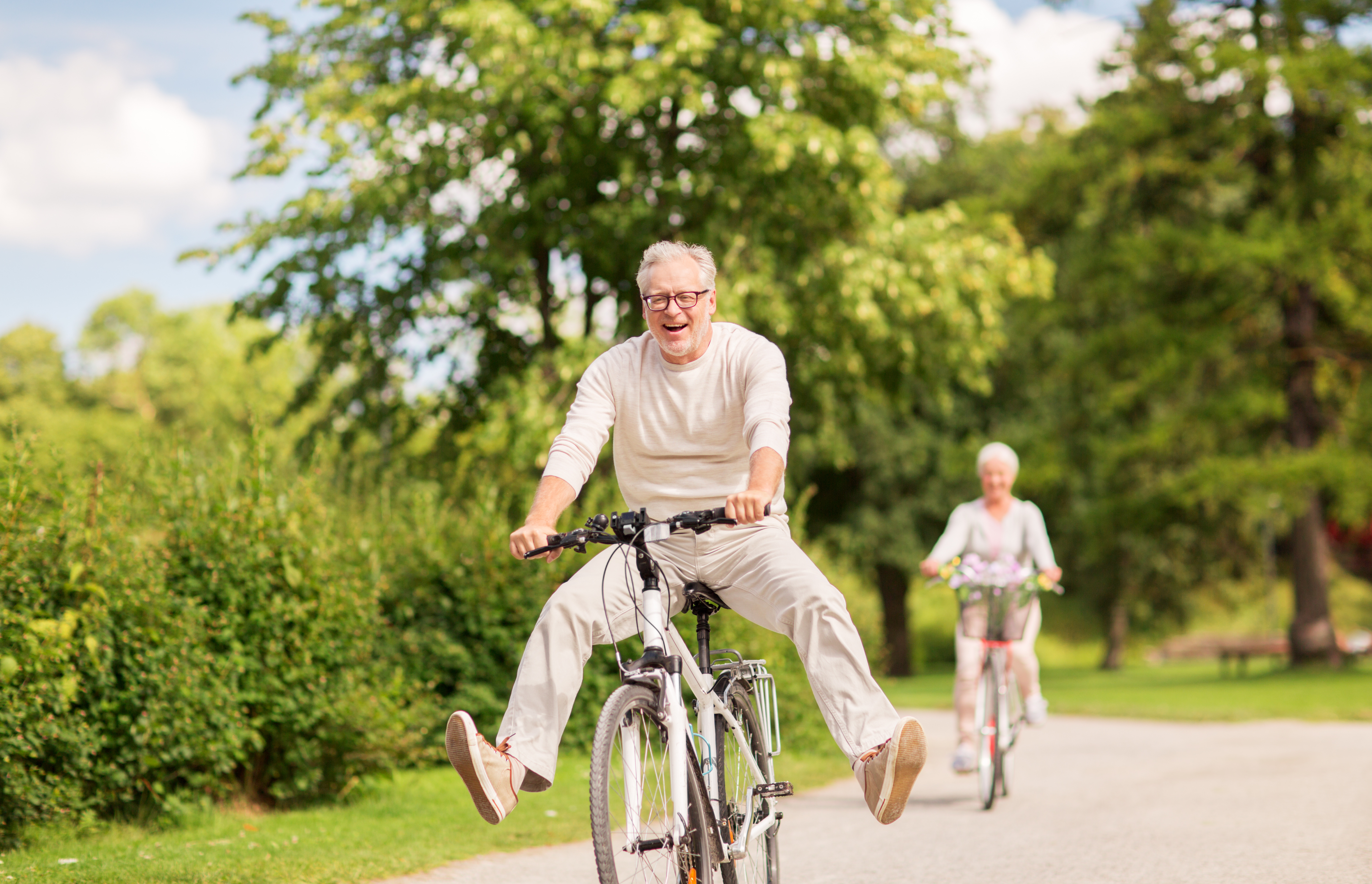 Older couple having fun cycling through a park on a summer's day